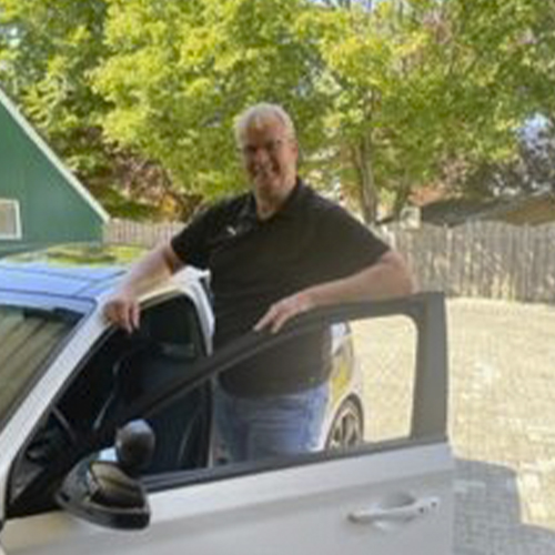 Hermann Behrens, Inhaber und Fahrlehrer der Fahrschule Schomaker-Behrens, an der geöffneten Fahrertür eines Fahrschulwagens